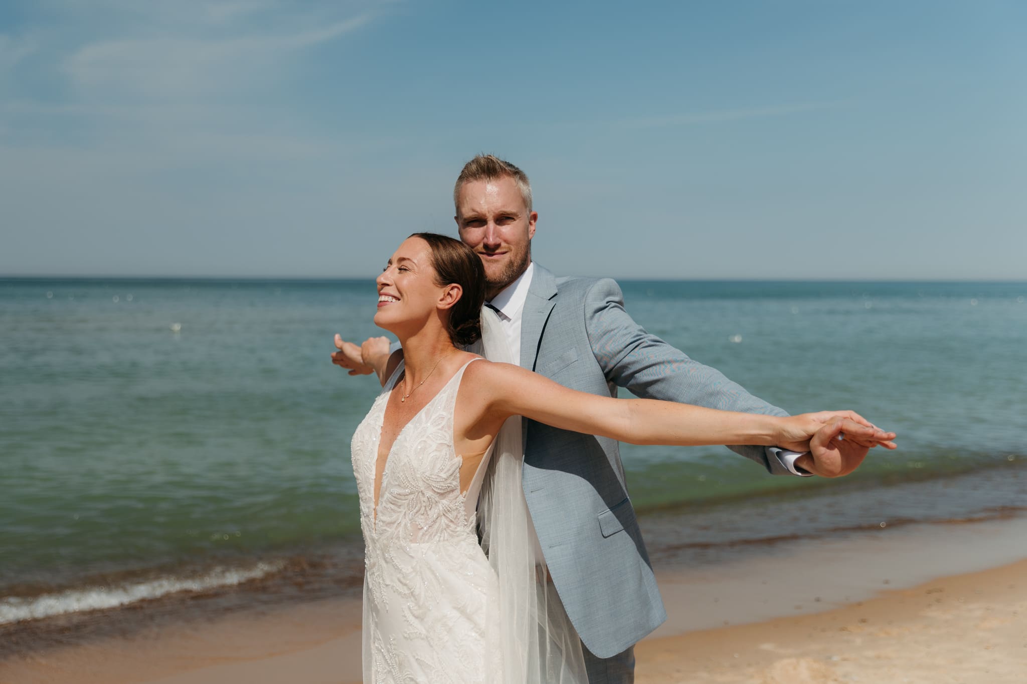 Bride and groom embrace while taking couple photos along the beach at their Warren Dunes State Park elopement