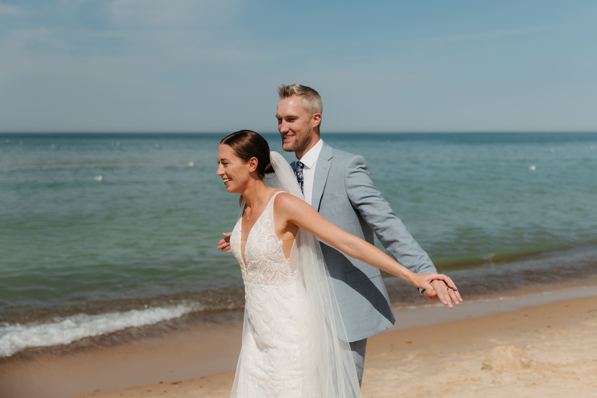 Bride and groom embrace while taking couple photos along the beach at their Warren Dunes State Park elopement