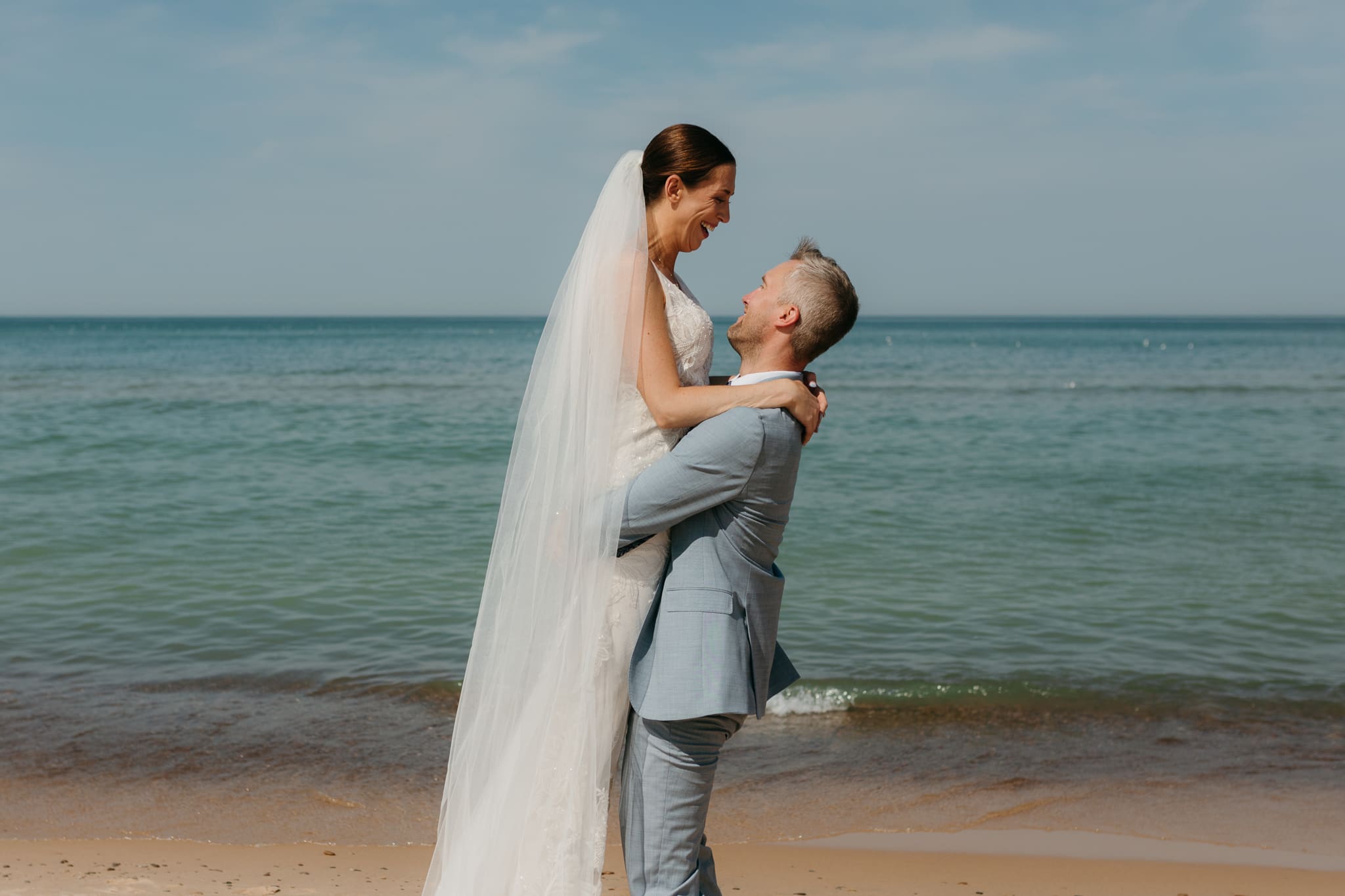 Bride and groom embrace while taking couple photos along the beach at their Warren Dunes State Park elopement