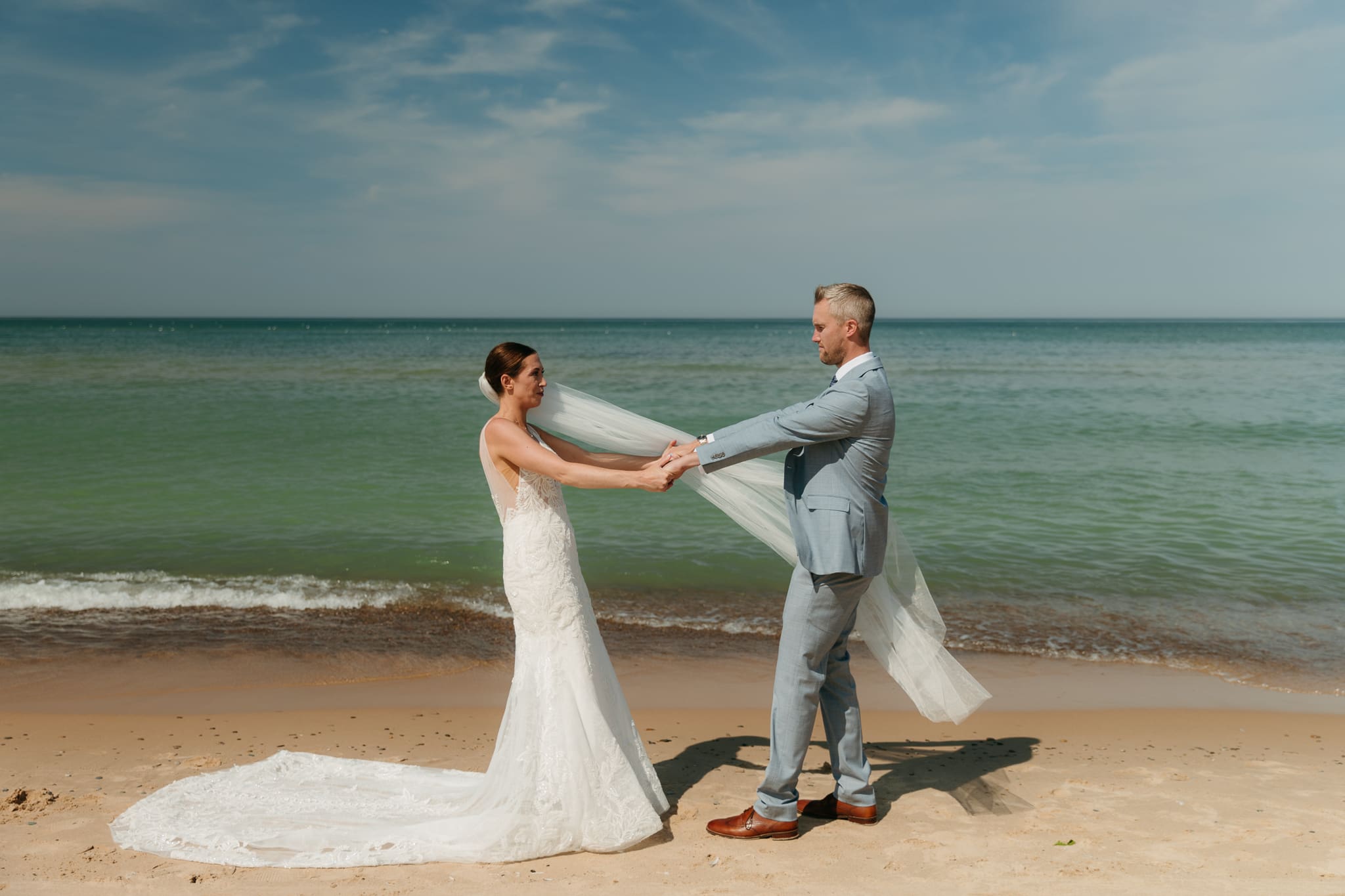 Bride and groom embrace while taking couple photos along the beach at their Warren Dunes State Park elopement