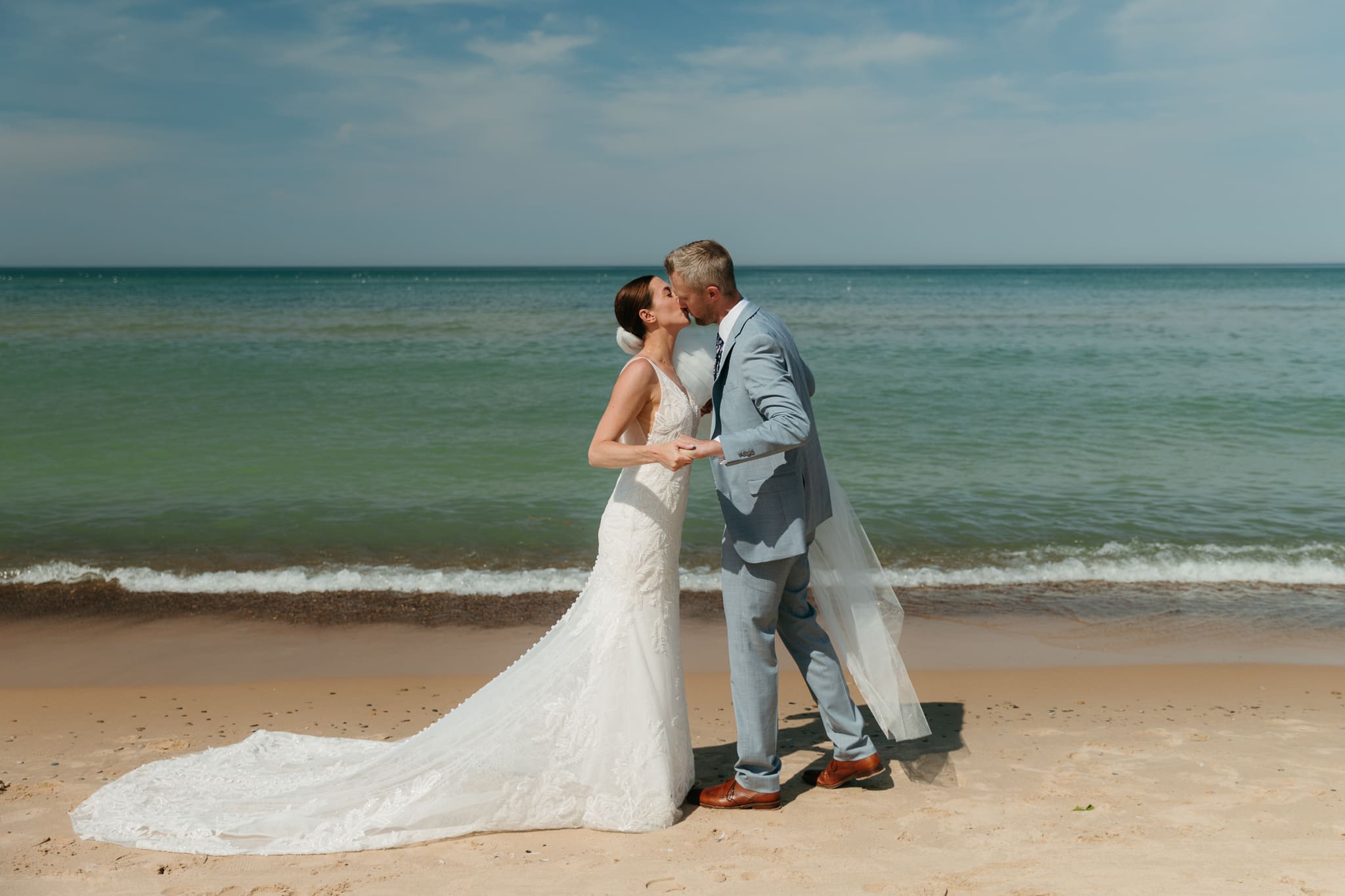 Bride and groom embrace while taking couple photos along the beach at their Warren Dunes State Park elopement