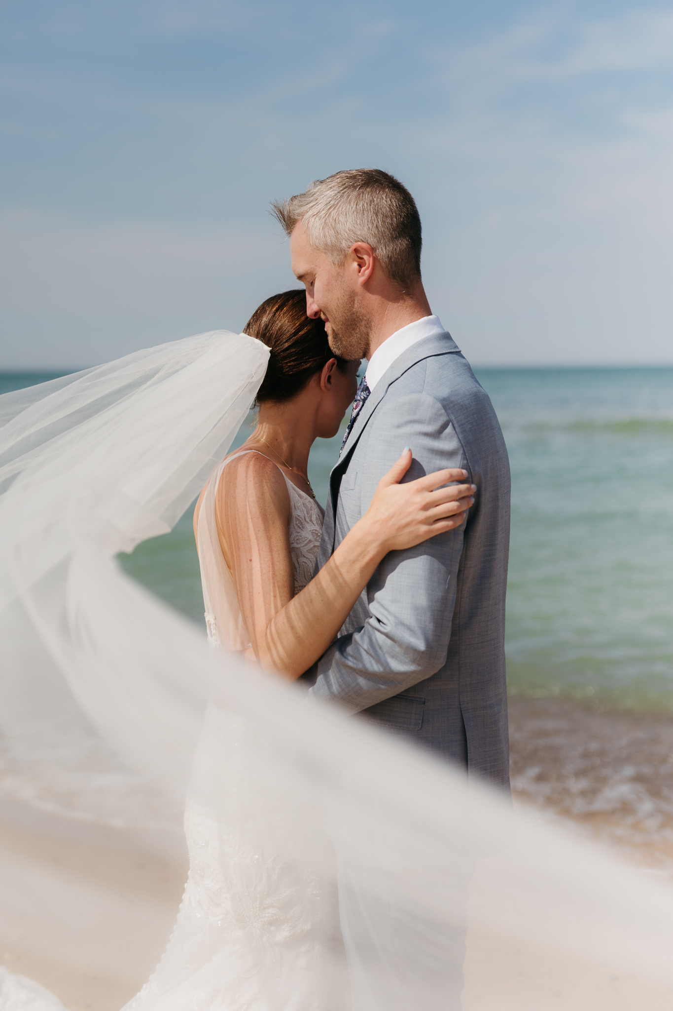 Bride and groom embrace while taking couple photos along the beach at their Warren Dunes State Park elopement