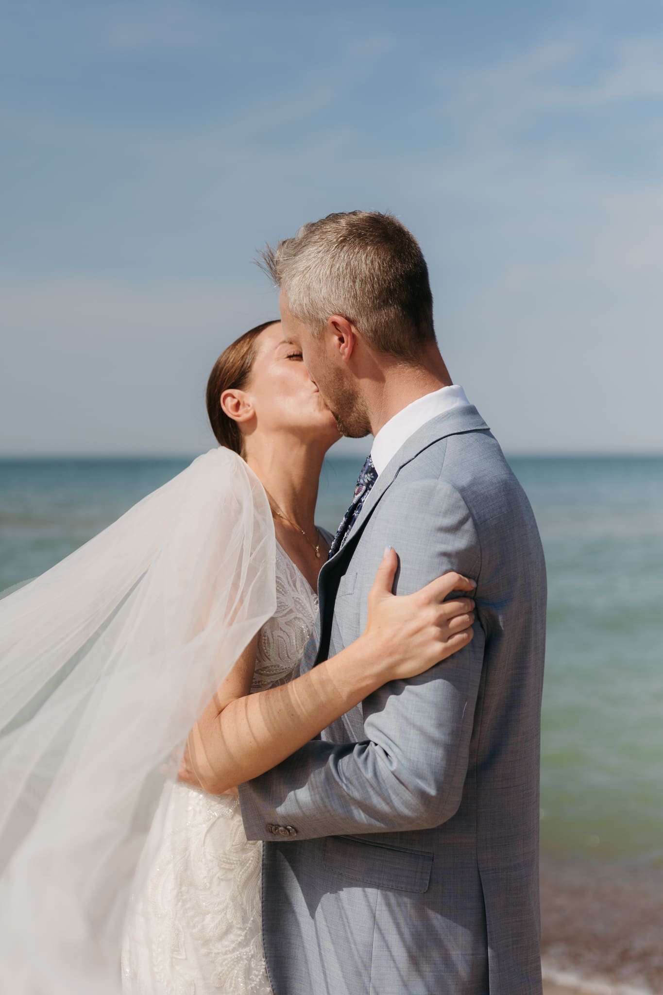 Bride and groom embrace while taking couple photos along the beach at their Warren Dunes State Park elopement