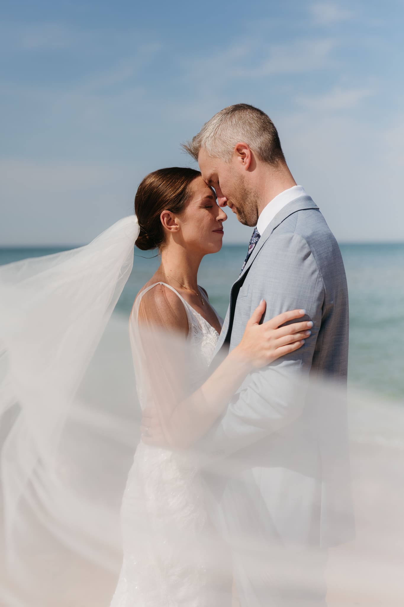 Bride and groom embrace while taking couple photos along the beach at their Warren Dunes State Park elopement