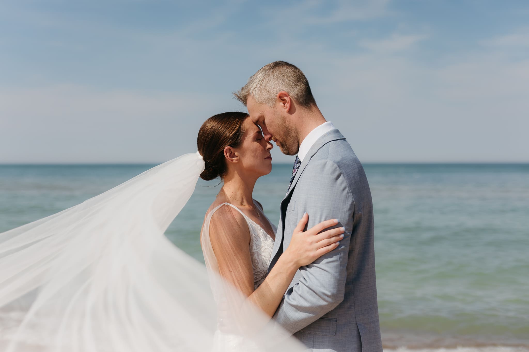 Bride and groom embrace while taking couple photos along the beach at their Warren Dunes State Park elopement