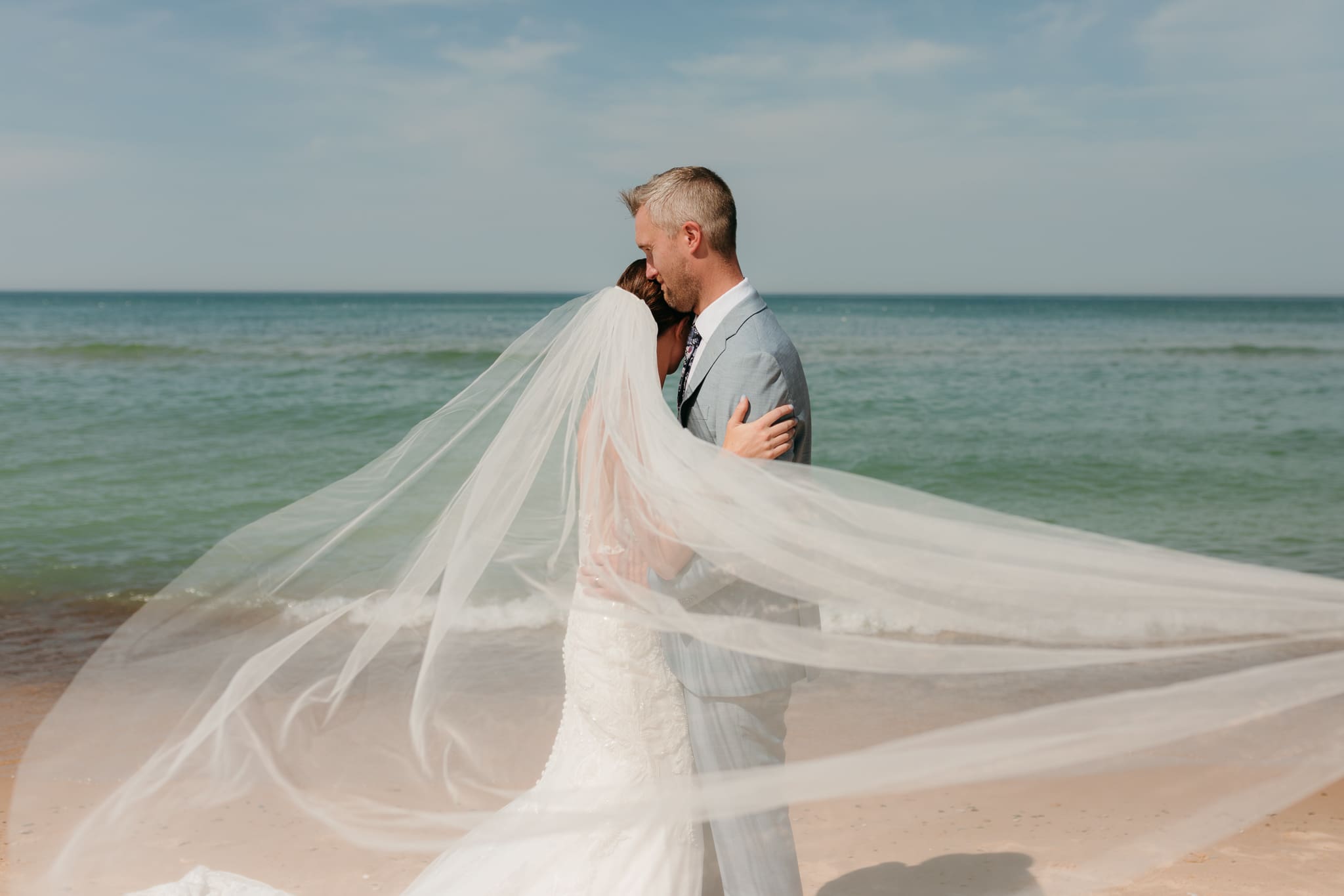 Bride and groom embrace while taking couple photos along the beach at their Warren Dunes State Park elopement