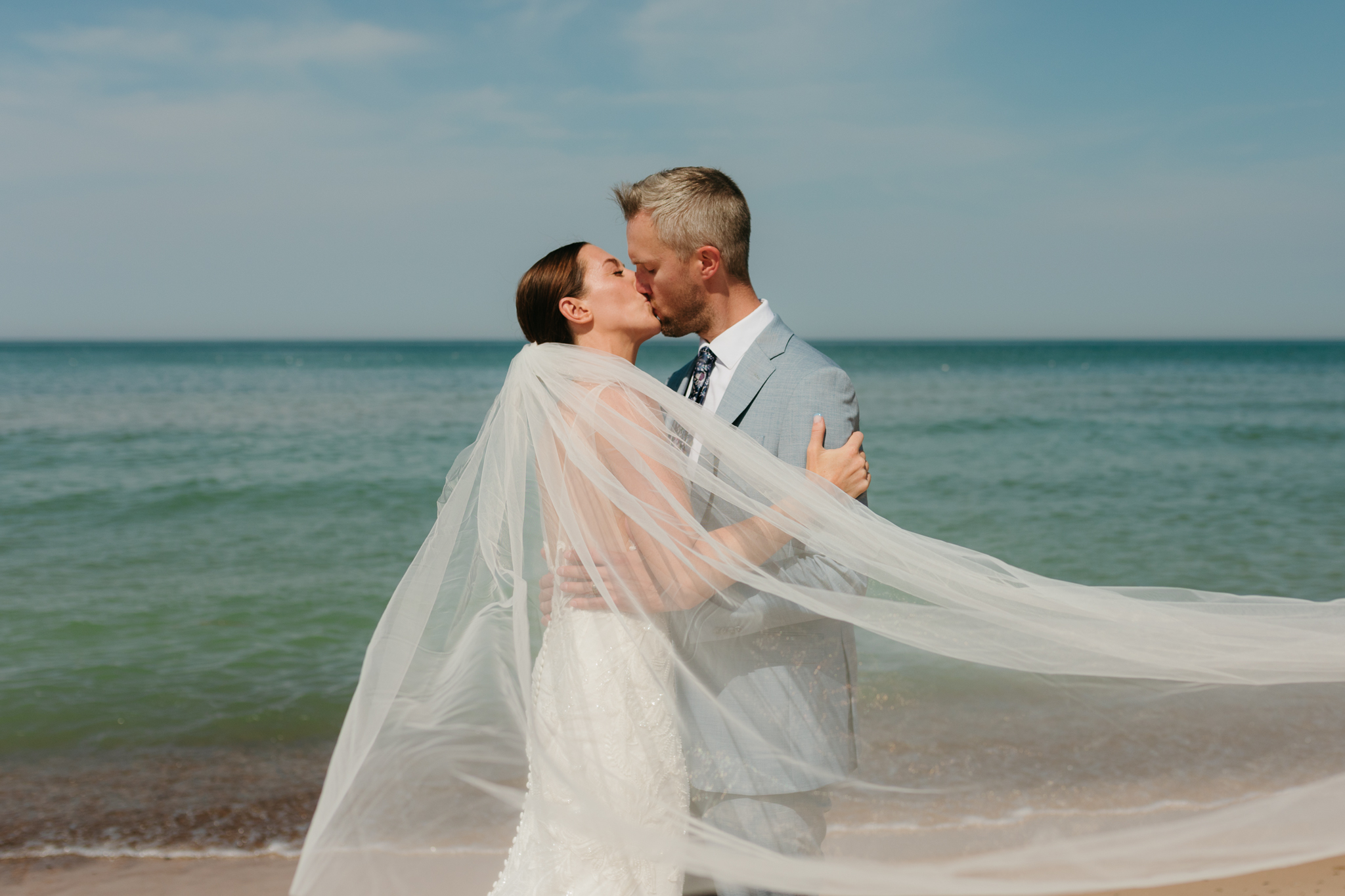 Bride and groom embrace while taking couple photos along the beach at their Warren Dunes State Park elopement