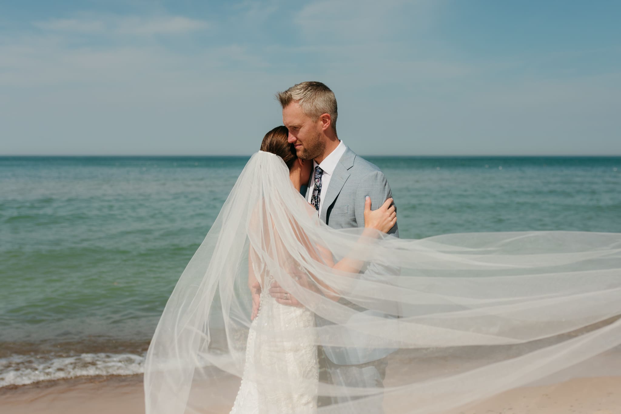 Bride and groom embrace while taking couple photos along the beach at their Warren Dunes State Park elopement