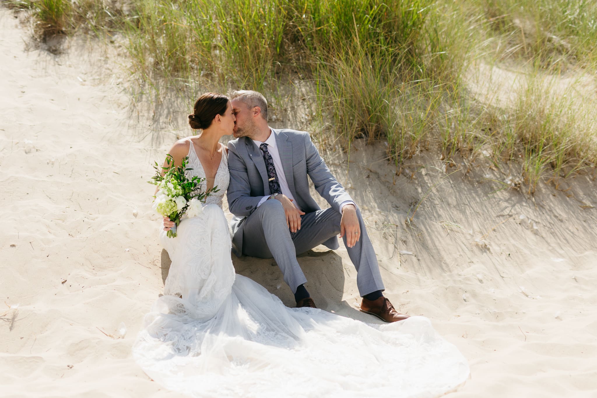 Bride and groom embrace and kiss next to sand dunes during their Lake Michigan elopement