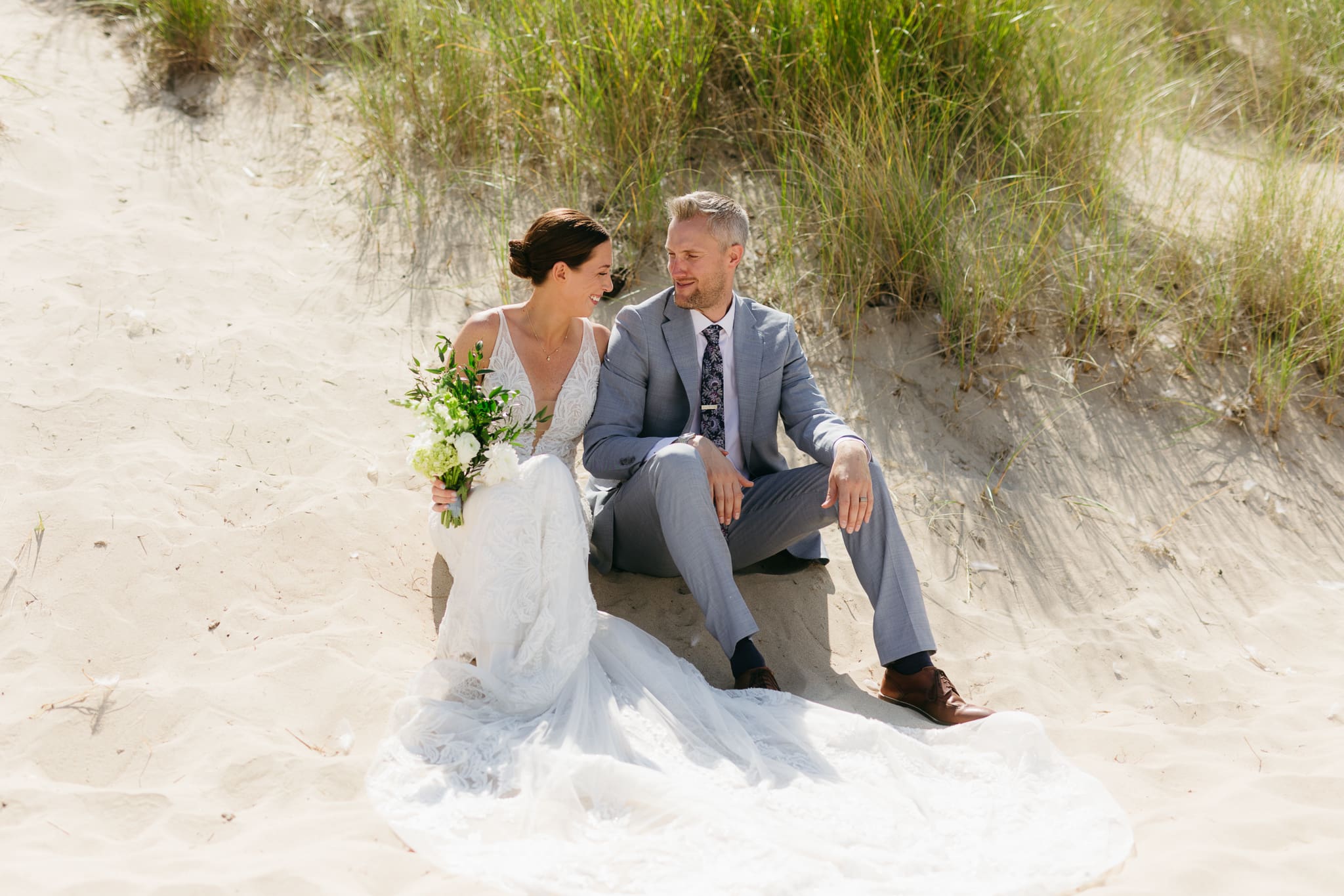 Bride and groom embrace and kiss next to sand dunes during their Lake Michigan elopement
