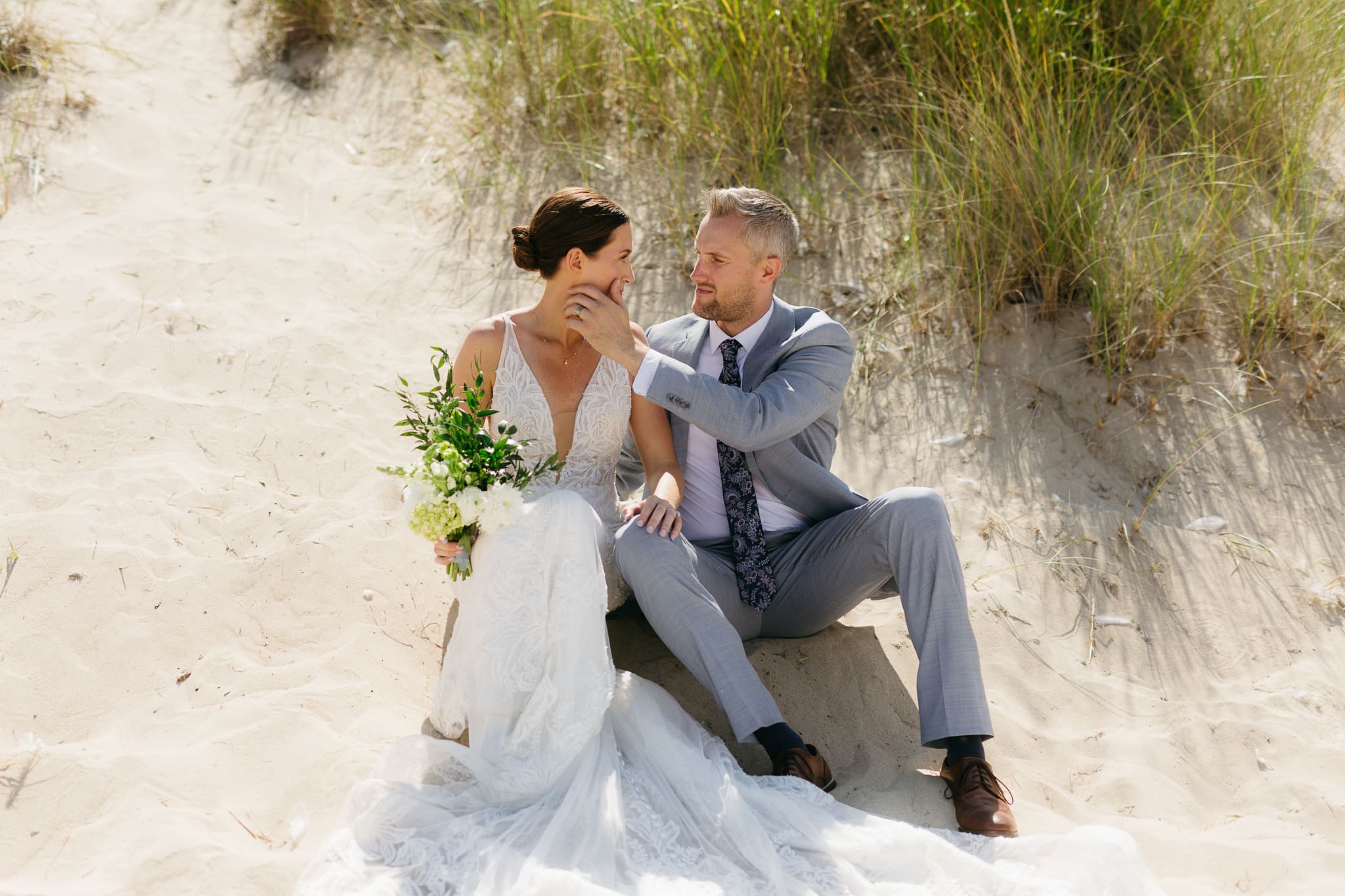 Bride and groom embrace and kiss next to sand dunes during their Lake Michigan elopement
