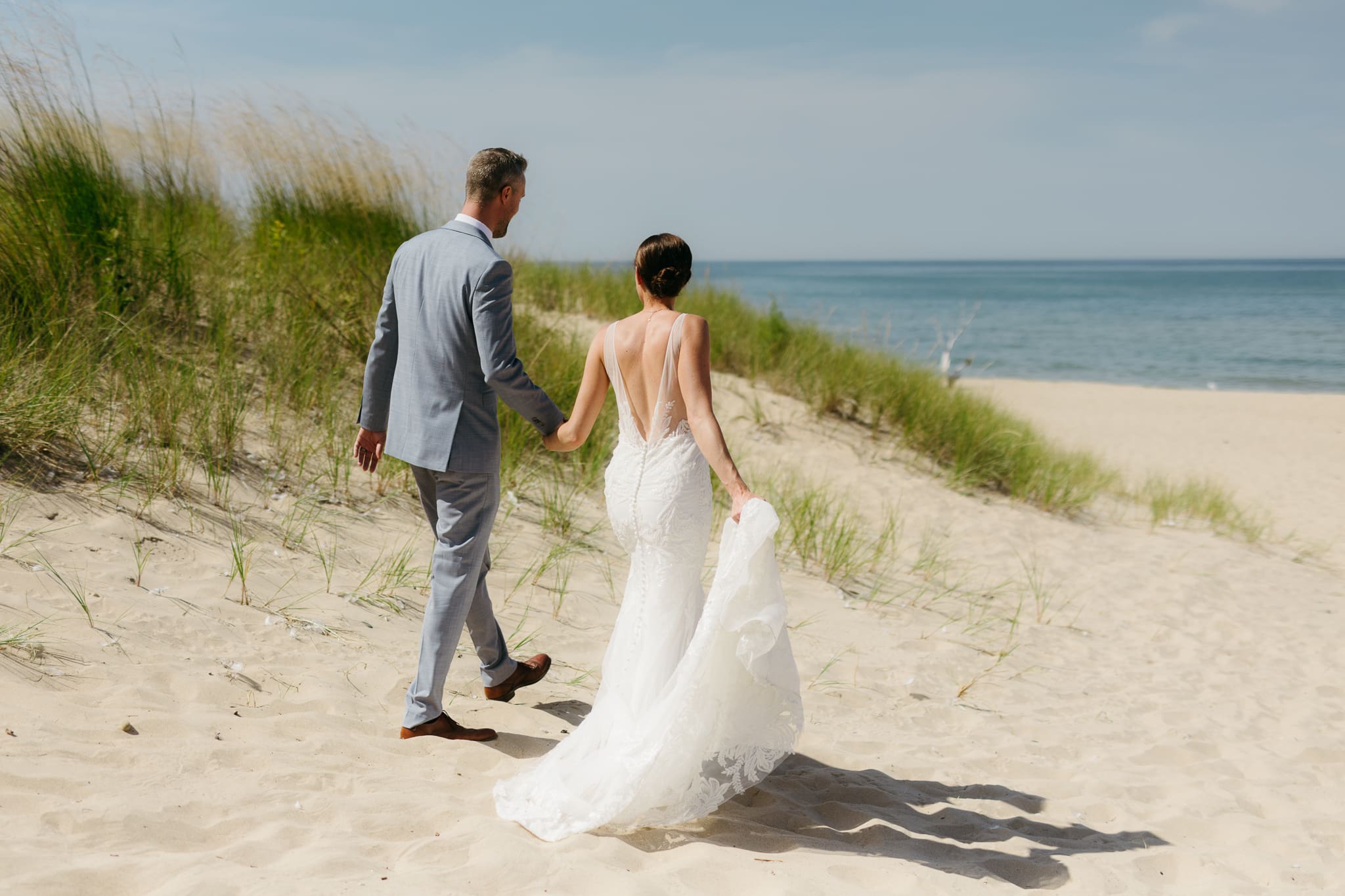 Bride and groom embrace and kiss next to sand dunes during their Lake Michigan elopement