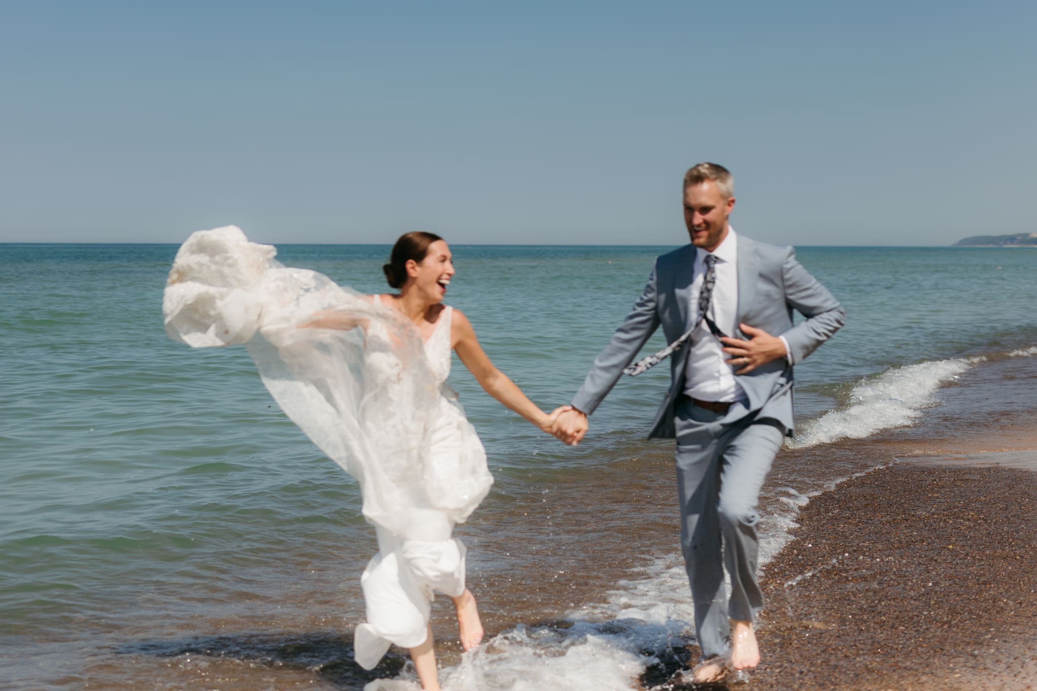 Bride and groom running along the shore of Lake Michigan during their elopement at Warren Dunes State Park