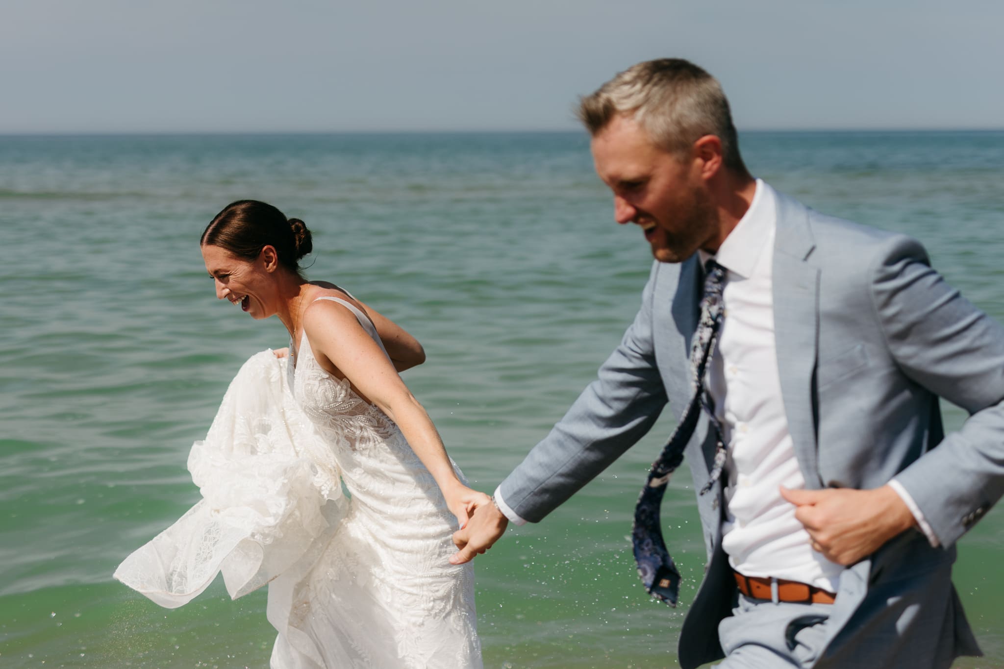 Bride and groom running along the shore of Lake Michigan during their elopement at Warren Dunes State Park