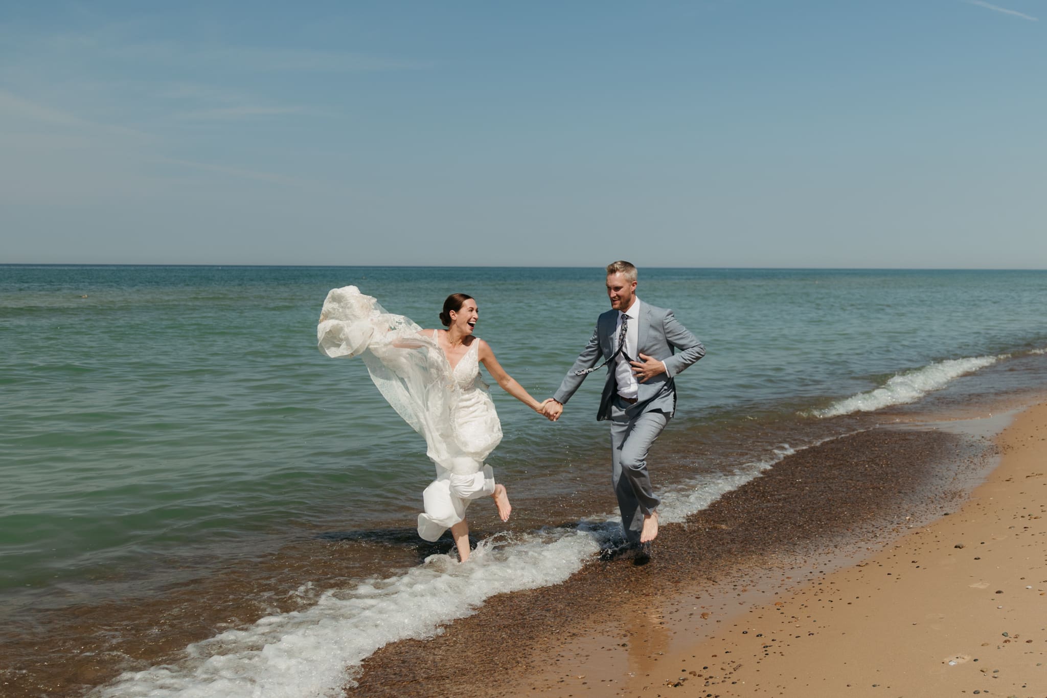 Bride and groom running along the shore of Lake Michigan during their elopement at Warren Dunes State Park
