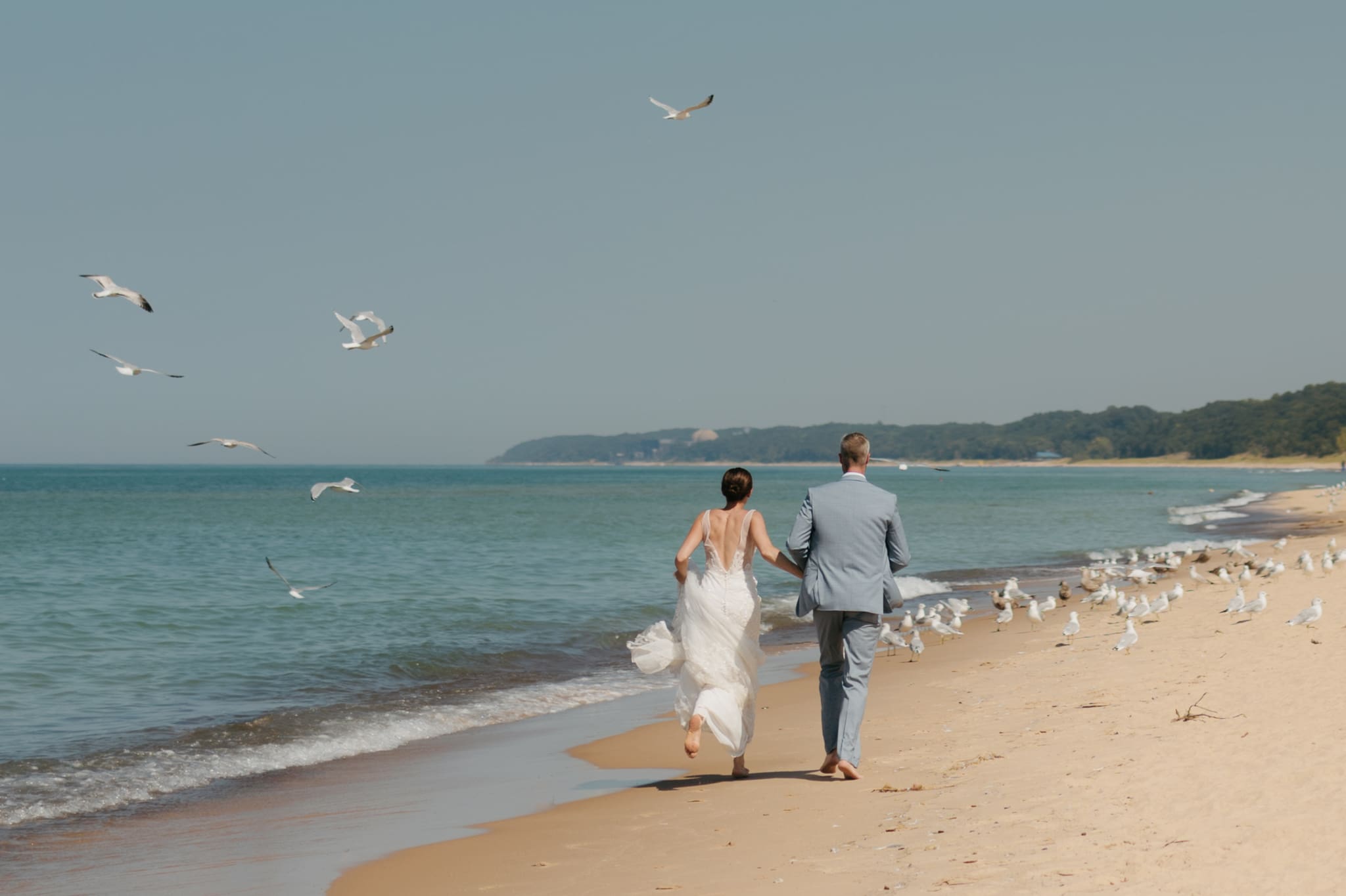 Bride and groom running along the beach of Lake Michigan through a flock of seagulls during their elopement at Warren Dunes State Park