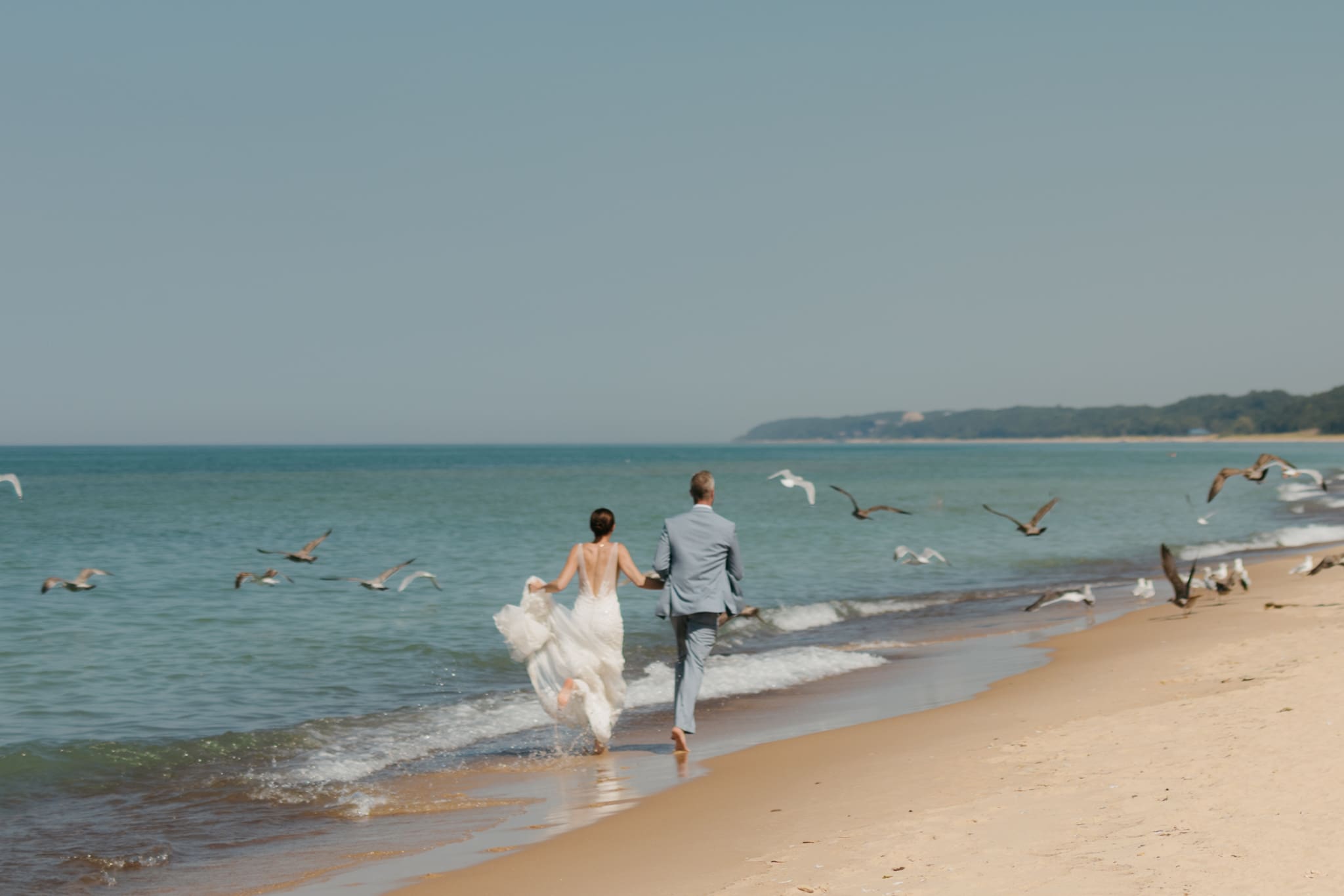 Bride and groom running along the beach of Lake Michigan through a flock of seagulls during their elopement at Warren Dunes State Park