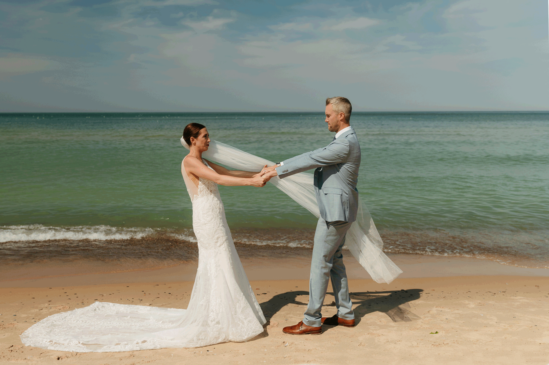 Bride and groom embrace while taking couple photos along the beach at their Warren Dunes State Park elopement