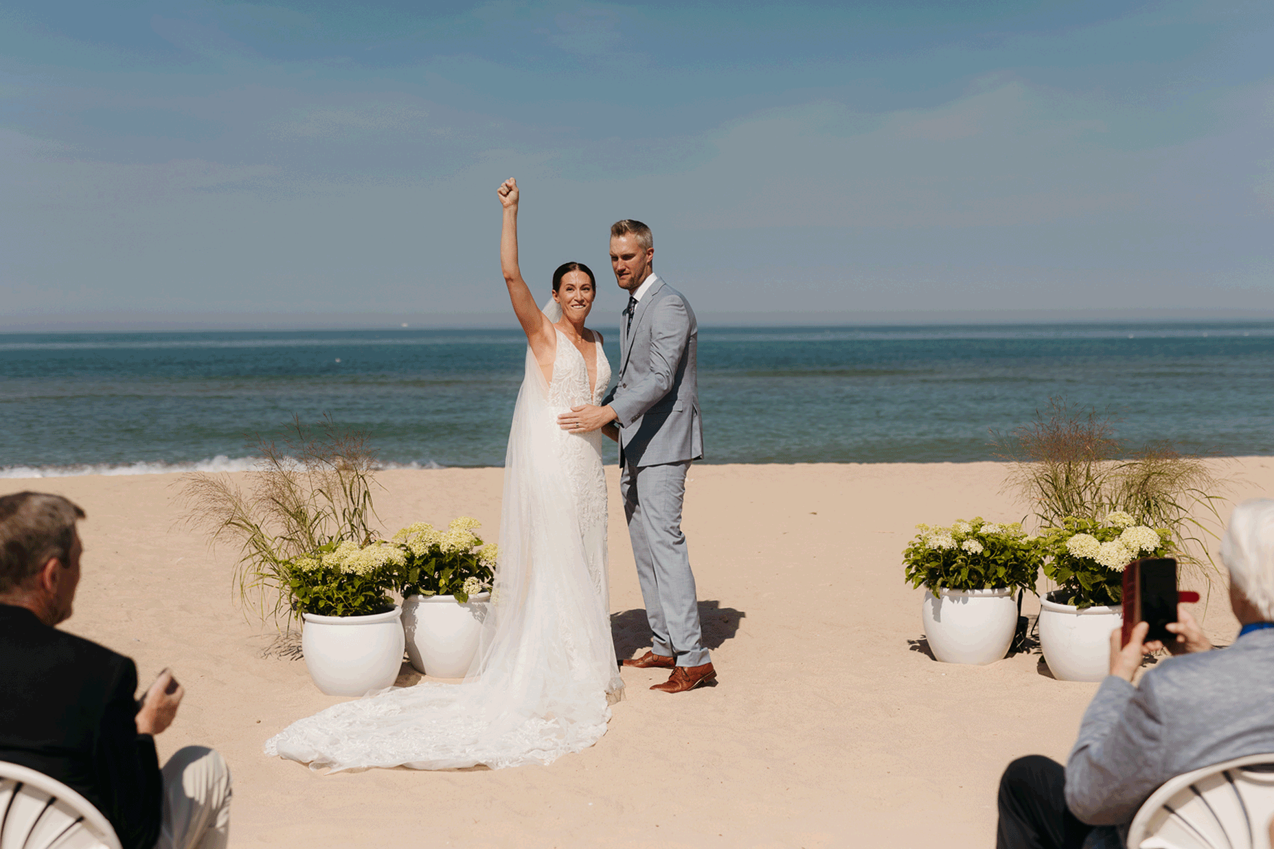 Bride and groom embrace and celebrate after sealing their wedding ceremony with a first kiss, during their Lake Michigan beach wedding