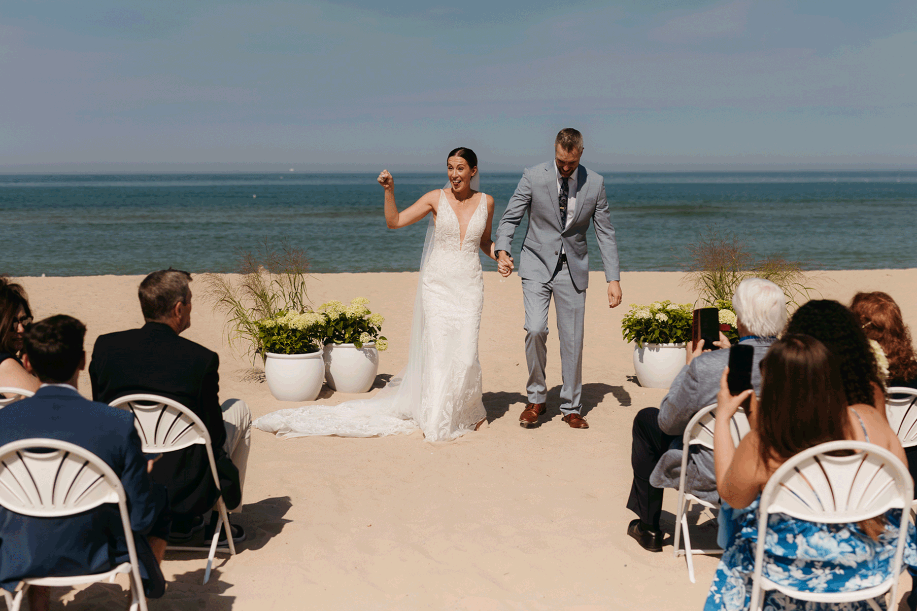 Bride and groom embrace and celebrate after sealing their wedding ceremony with a first kiss, during their Lake Michigan beach wedding