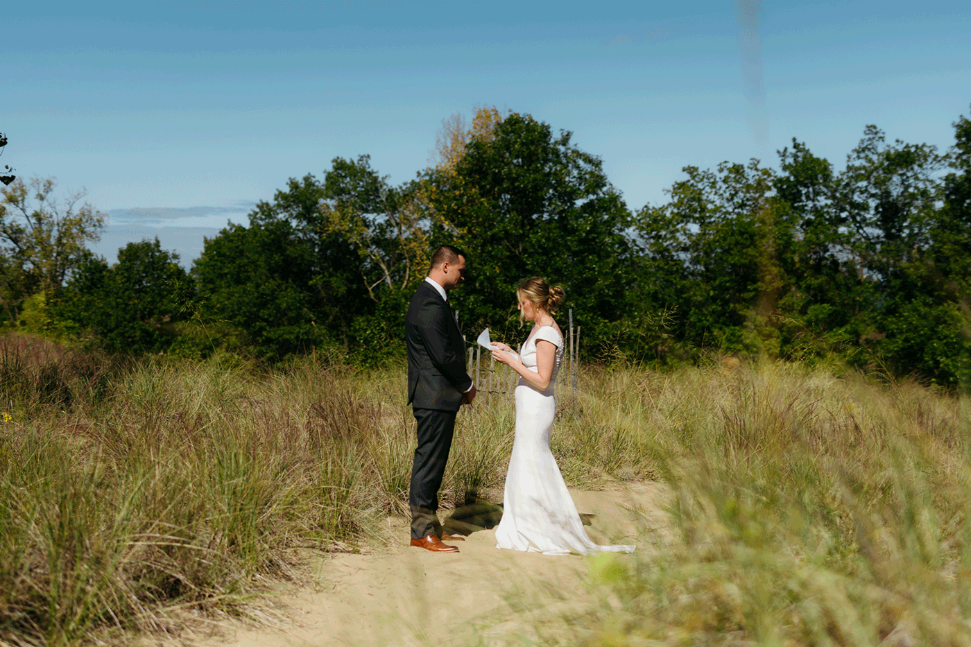 Bride and groom exchange private vows among the dunes of Indiana Dunes National Park, with dune grass swaying in the breeze.