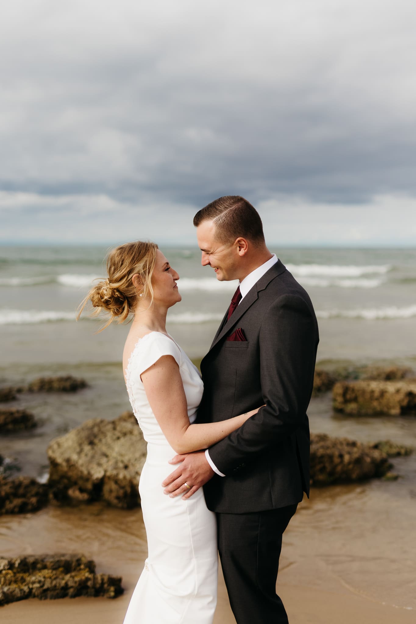 Bride and groom embrace and take couple portraits together along the beach of Lake Michigan during their Indiana Dunes National Park wedding.