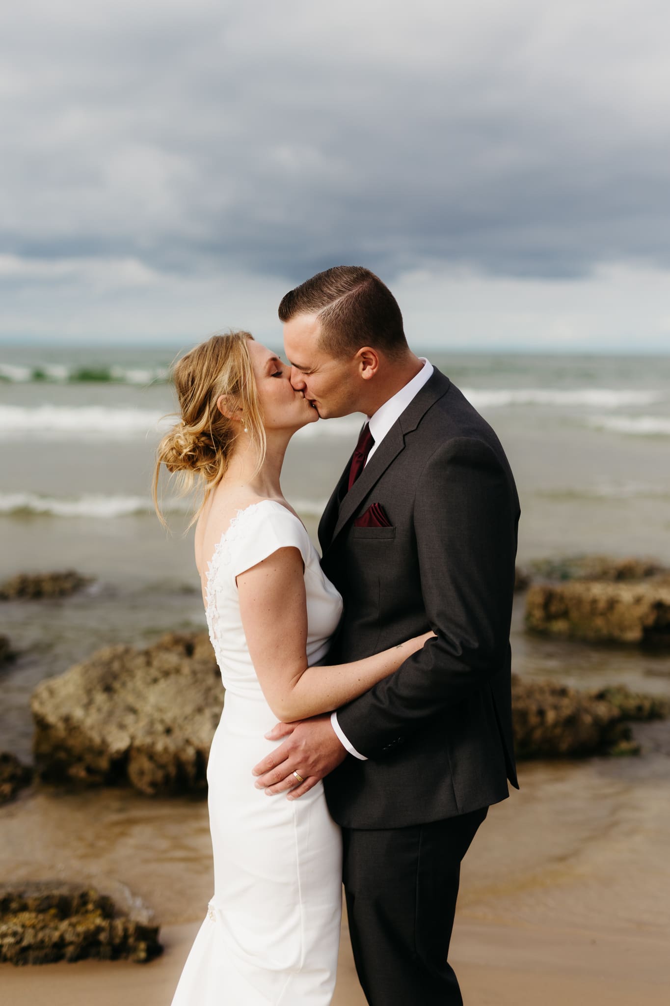 Bride and groom embrace and take couple portraits together along the beach of Lake Michigan during their Indiana Dunes National Park wedding.
