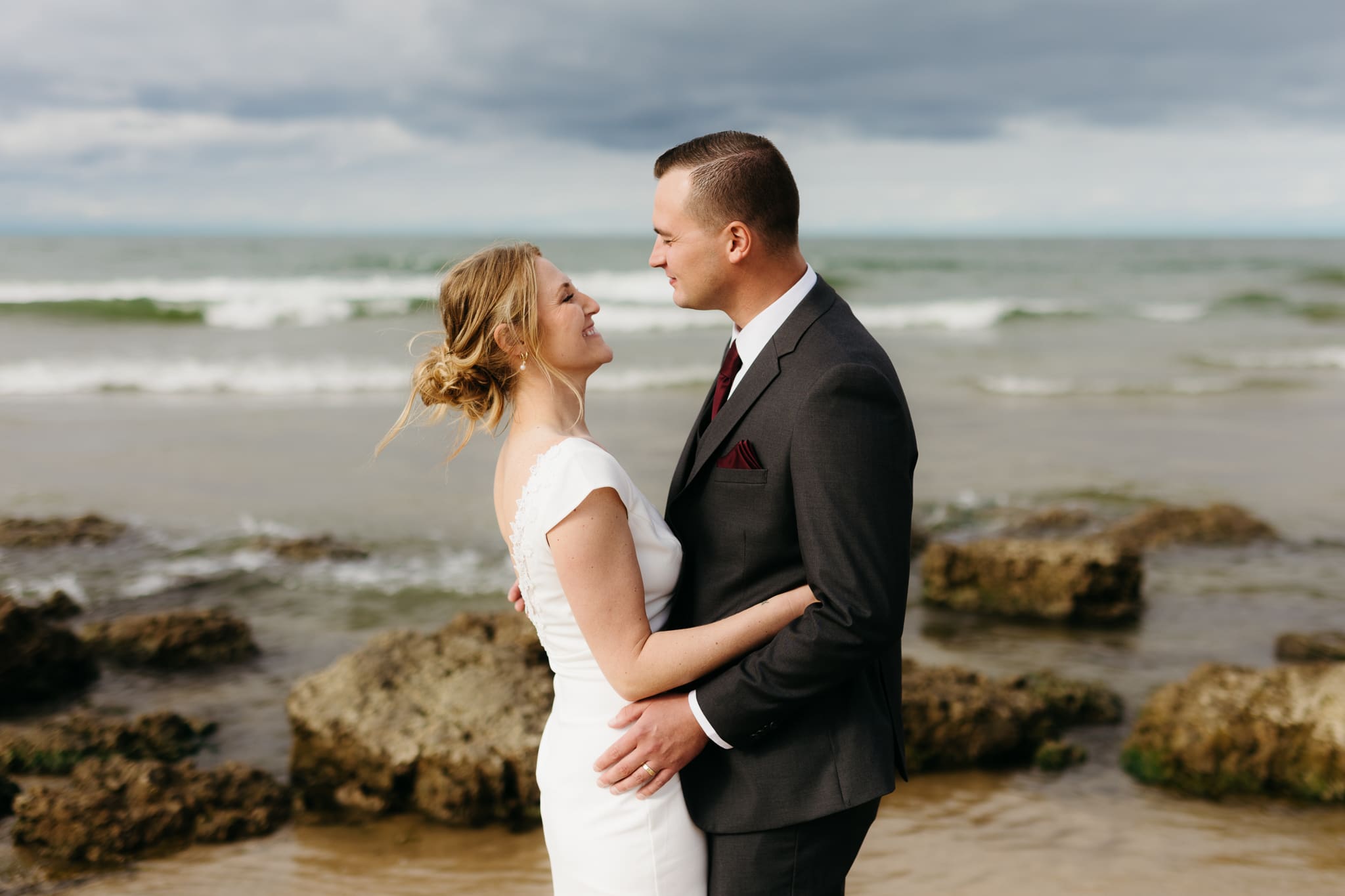Bride and groom embrace and take couple portraits together along the beach of Lake Michigan during their Indiana Dunes National Park wedding.