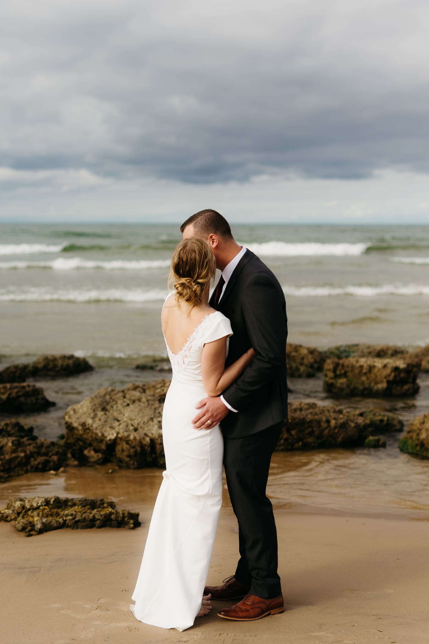 Bride and groom embrace and take couple portraits together along the beach of Lake Michigan during their Indiana Dunes National Park wedding.