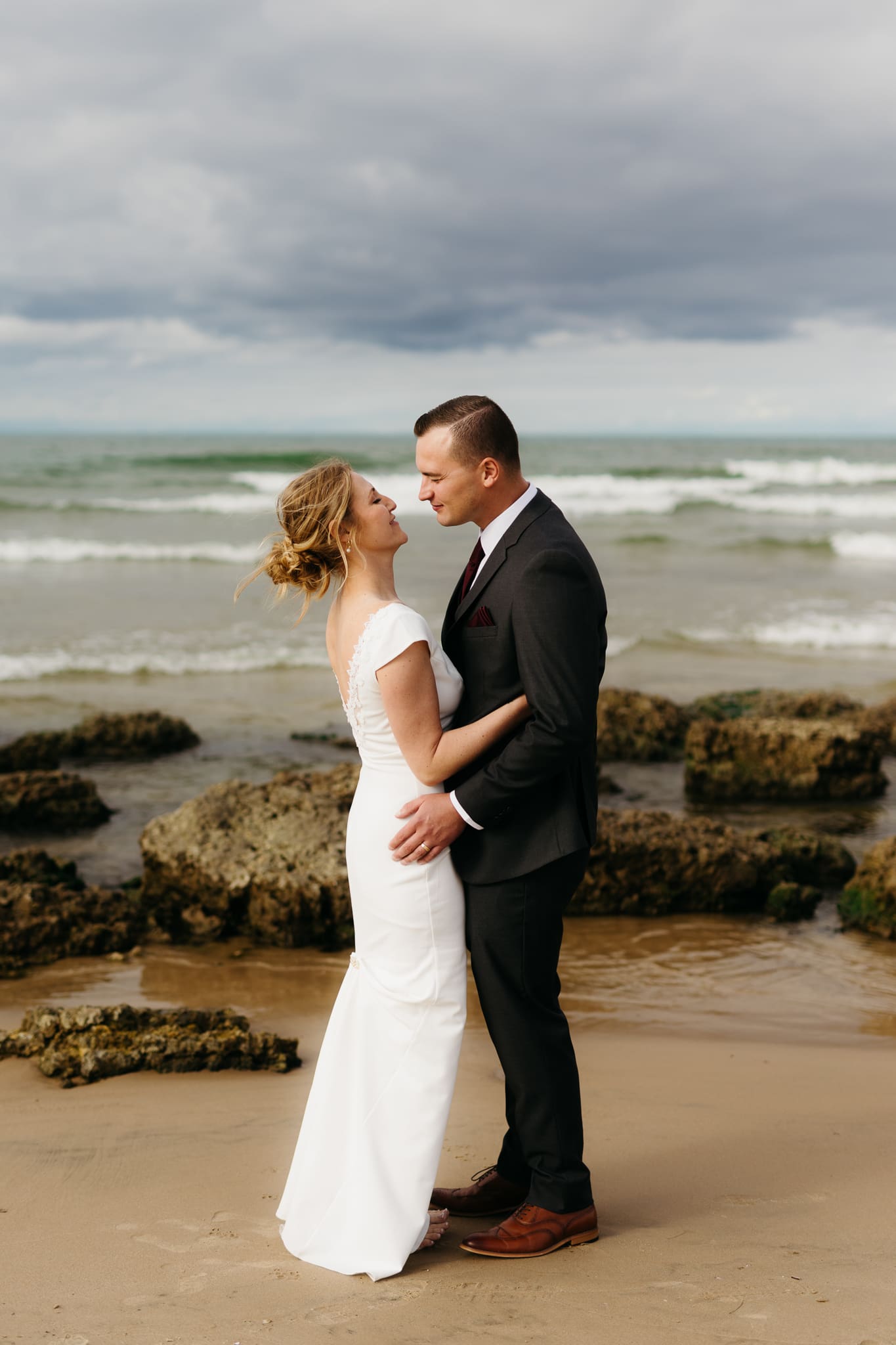 Bride and groom embrace and take couple portraits together along the beach of Lake Michigan during their Indiana Dunes National Park wedding.