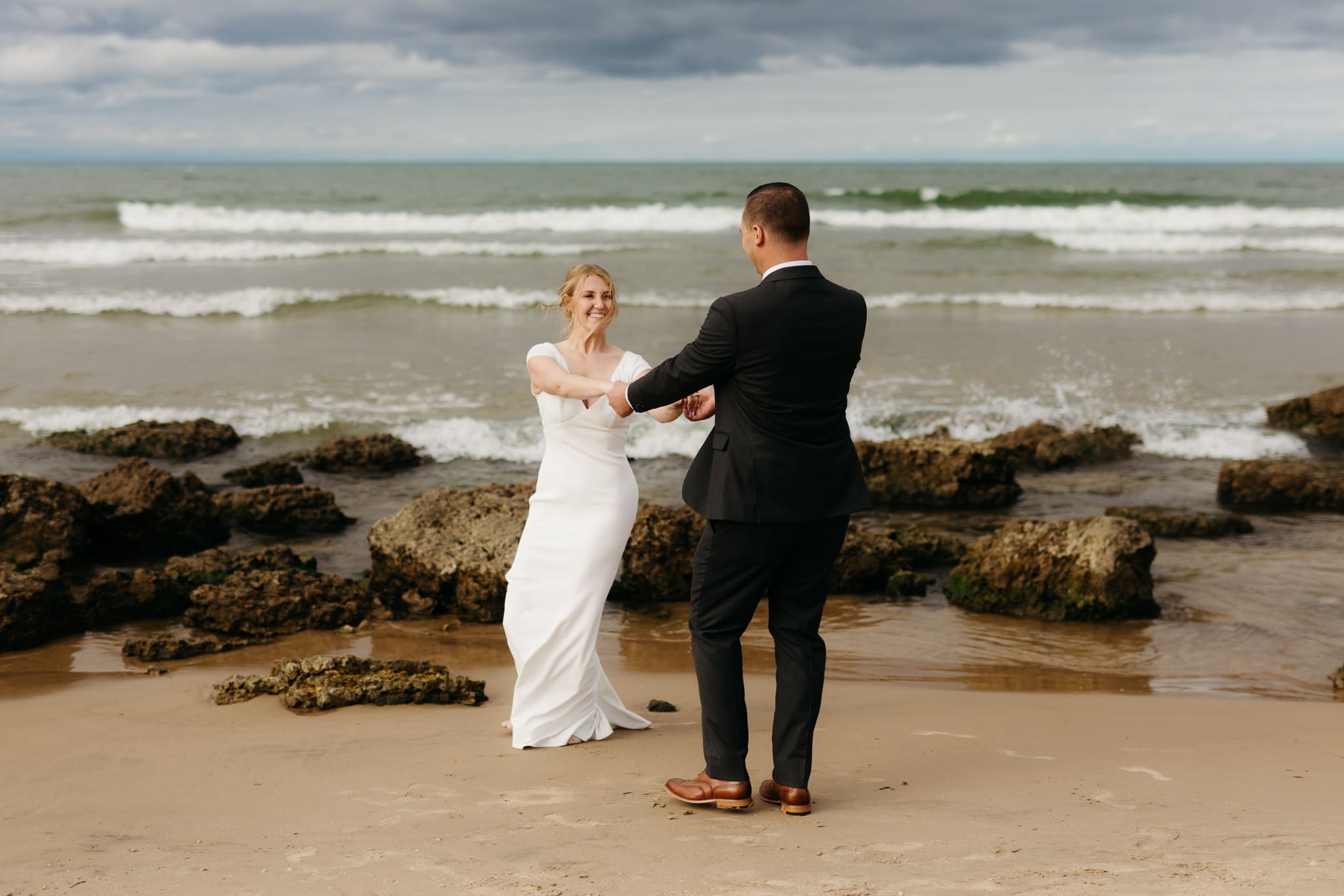 Bride and groom embrace and take couple portraits together along the beach of Lake Michigan during their Indiana Dunes National Park wedding.