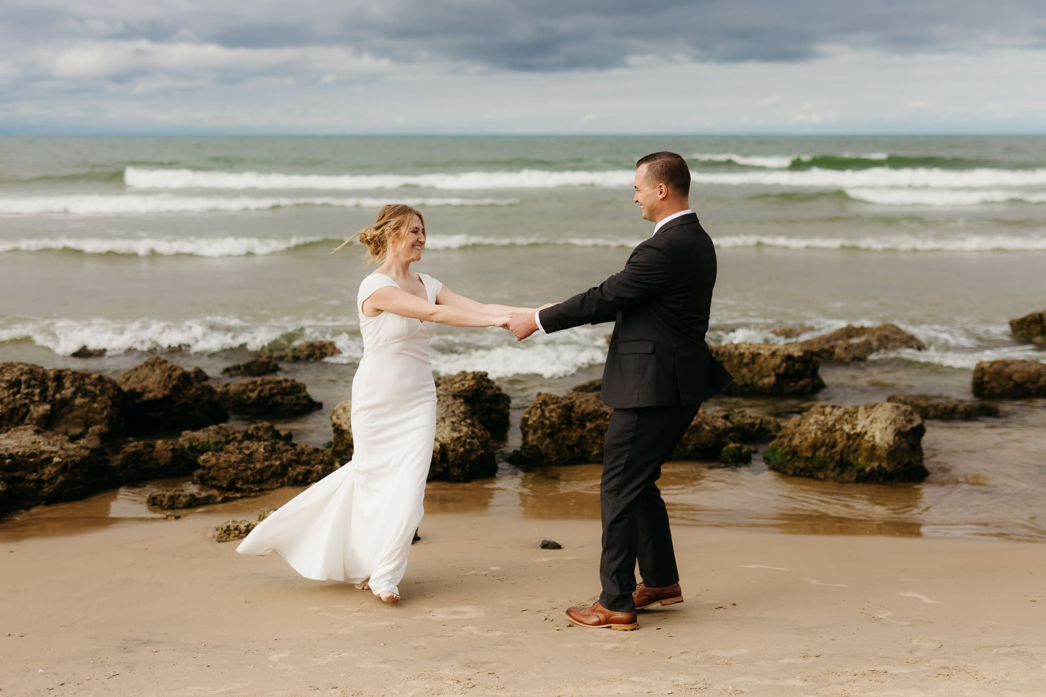 Bride and groom embrace and take couple portraits together along the beach of Lake Michigan during their Indiana Dunes National Park wedding.