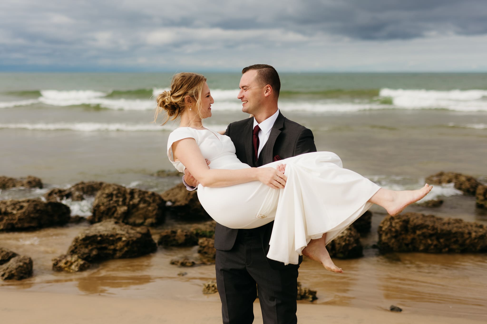 Bride and groom embrace and take couple portraits together along the beach of Lake Michigan during their Indiana Dunes National Park wedding.
