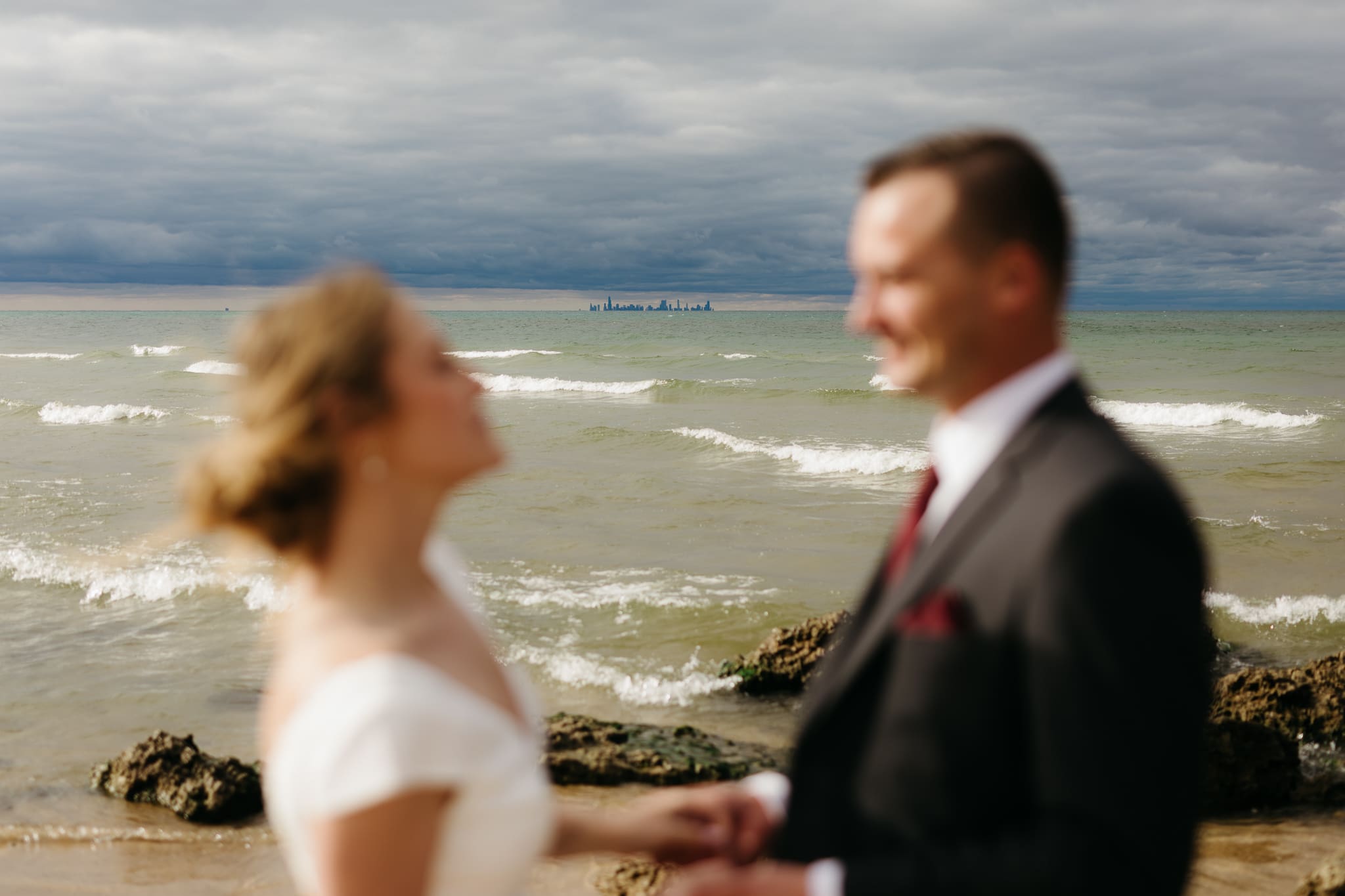 The skyline of Chicago in between a bride and groom smiling at each other during their wedding at Indiana Dunes National Park
