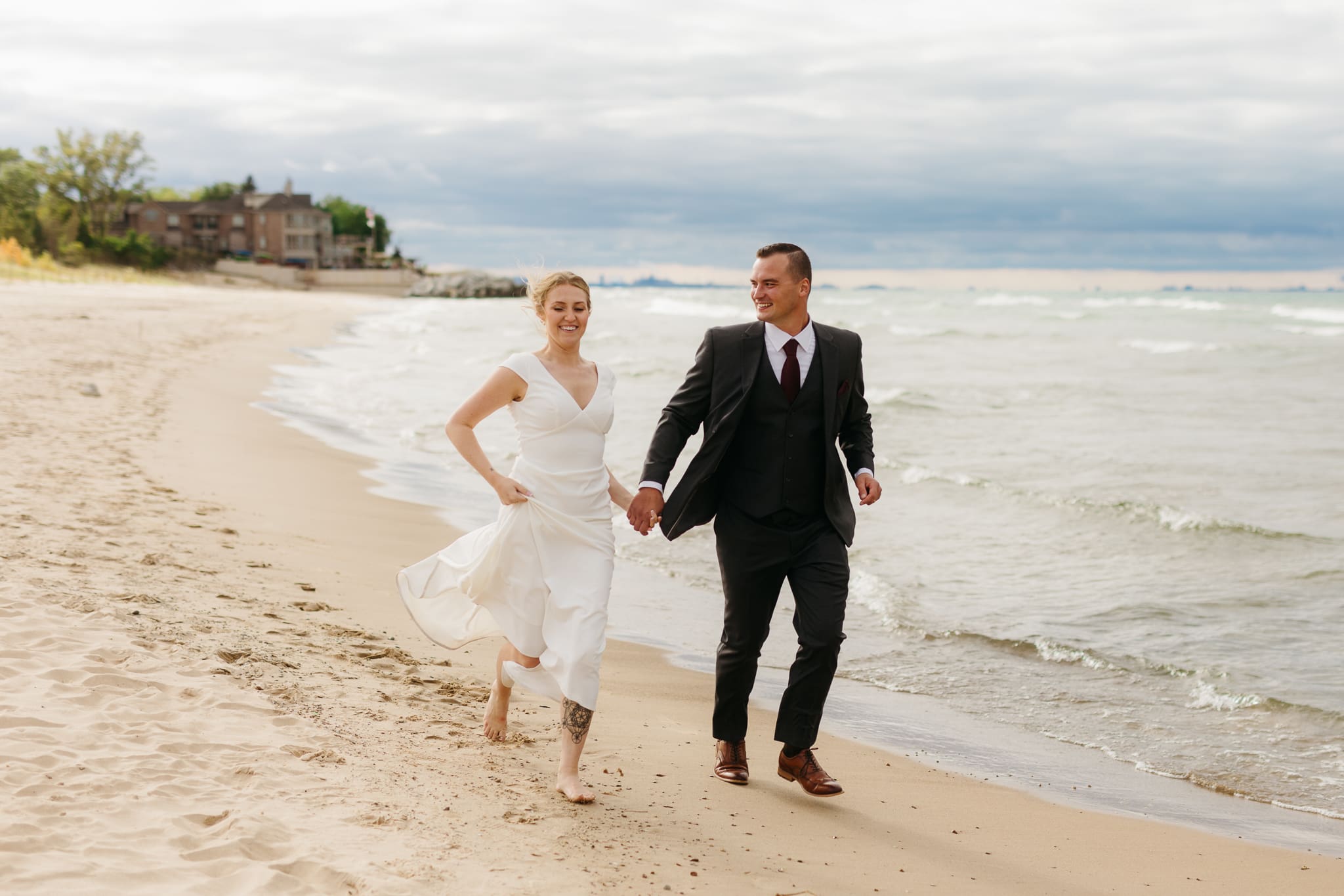 Bride and groom embrace and take couple portraits together along the beach of Lake Michigan during their Indiana Dunes National Park wedding.