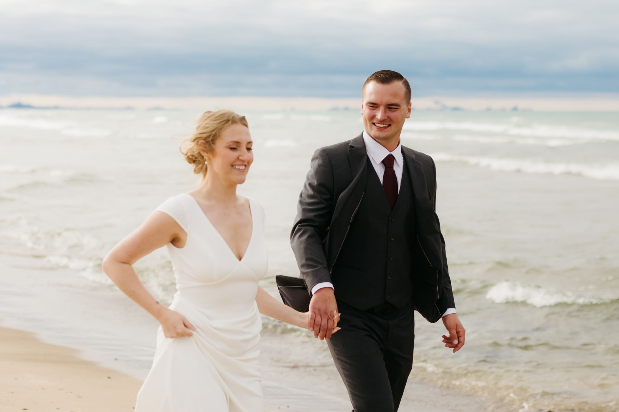 Bride and groom embrace and take couple portraits together along the beach of Lake Michigan during their Indiana Dunes National Park wedding.