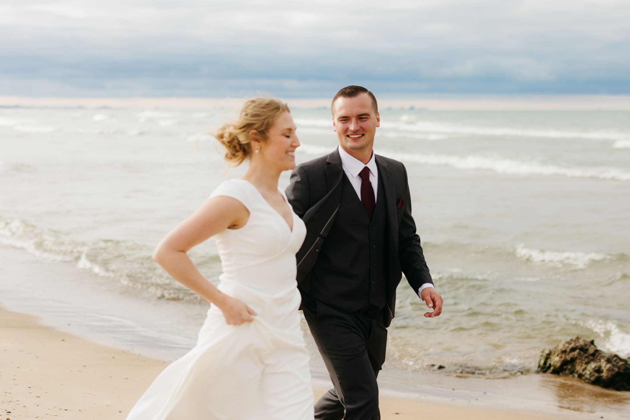 Bride and groom embrace and take couple portraits together along the beach of Lake Michigan during their Indiana Dunes National Park wedding.