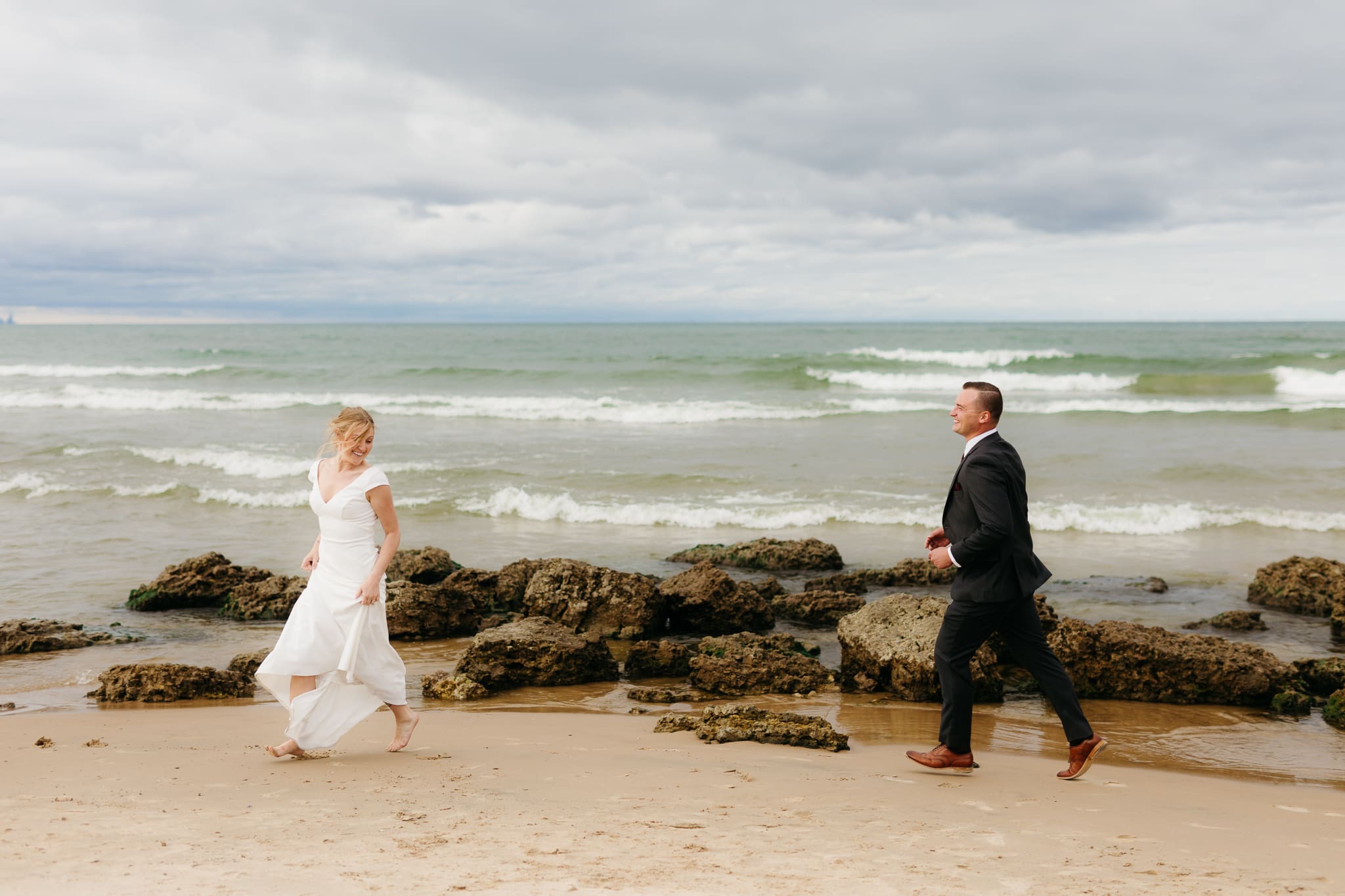Bride and groom embrace and take couple portraits together along the beach of Lake Michigan during their Indiana Dunes National Park wedding.