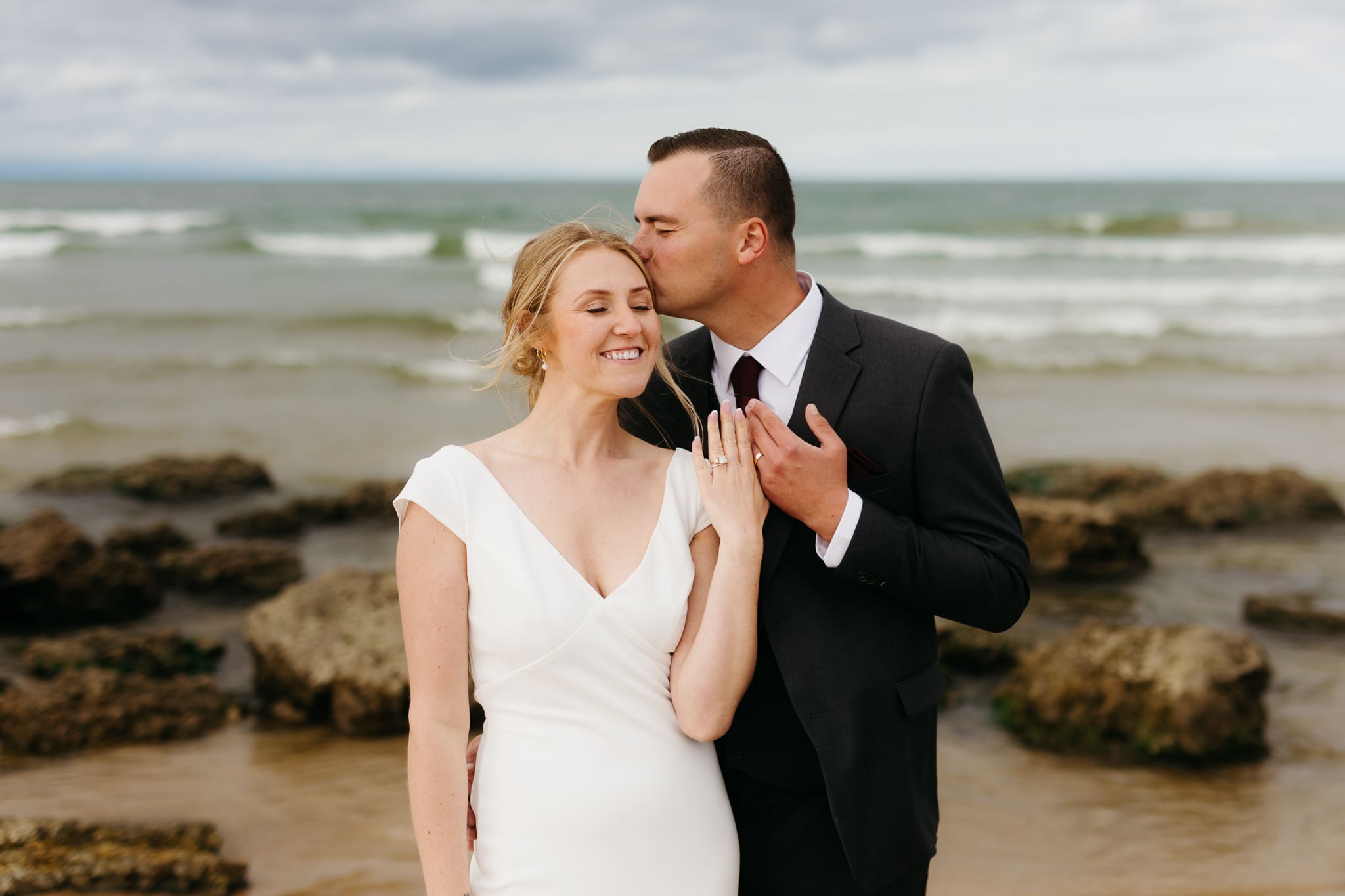 Bride and groom embrace and take couple portraits together along the beach of Lake Michigan during their Indiana Dunes National Park wedding.