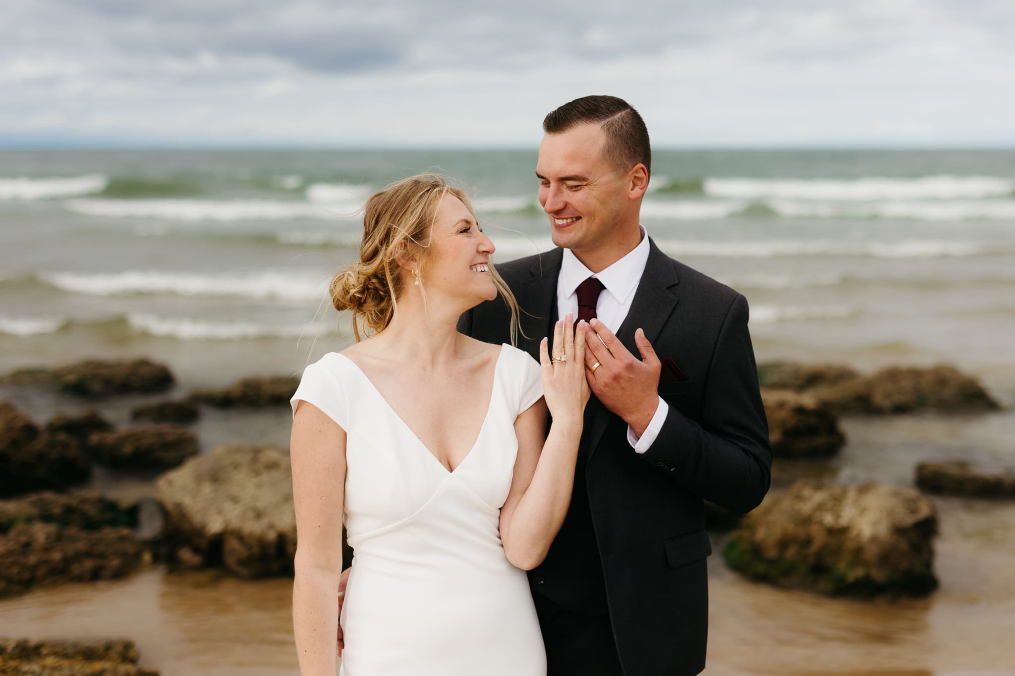 Bride and groom embrace and take couple portraits together along the beach of Lake Michigan during their Indiana Dunes National Park wedding.