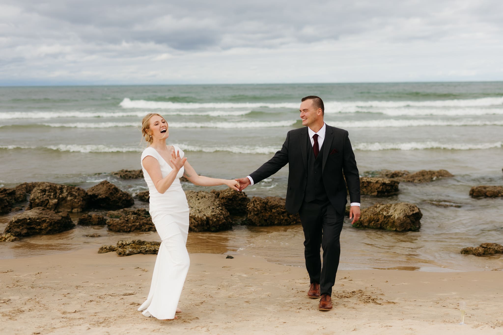 Bride and groom embrace and take couple portraits together along the beach of Lake Michigan during their Indiana Dunes National Park wedding.
