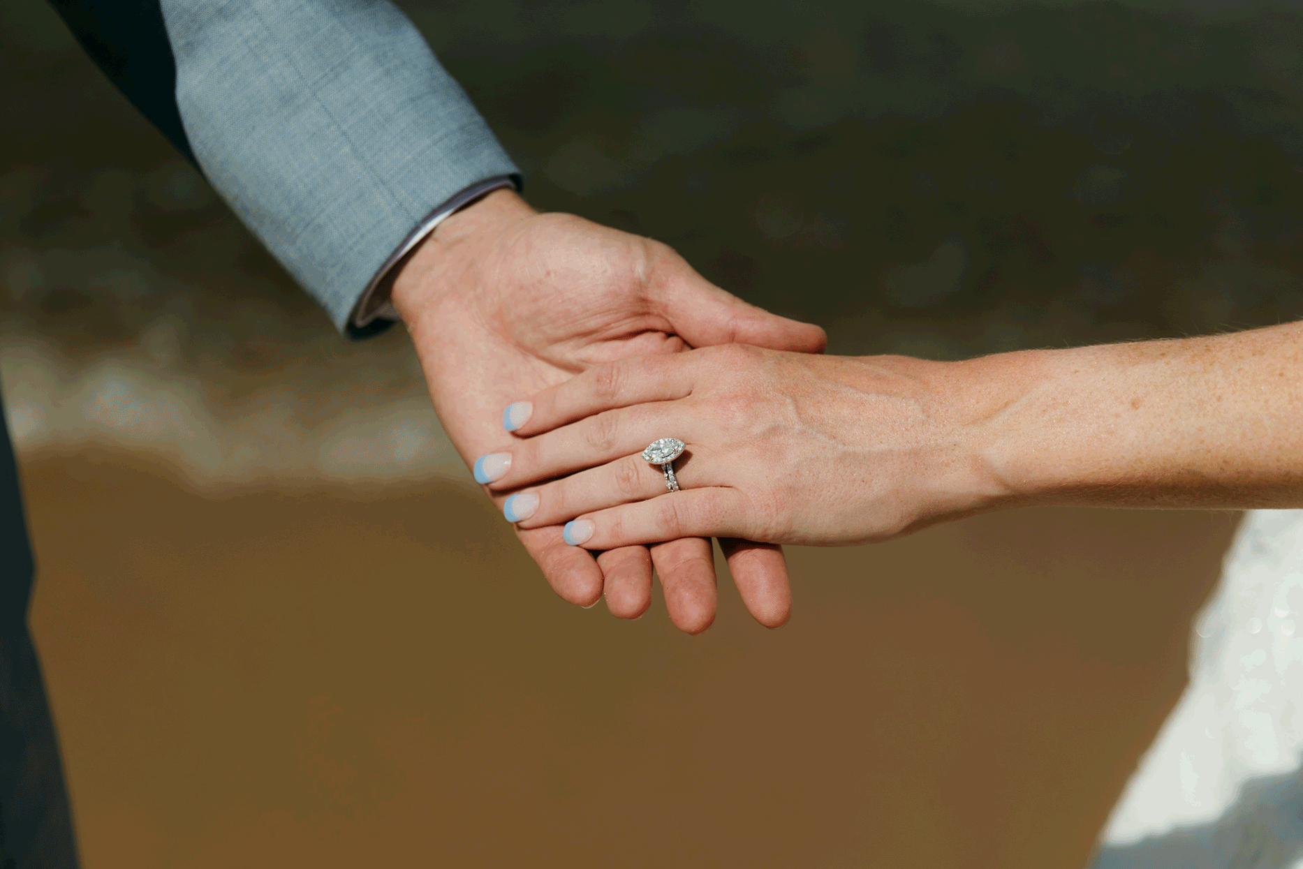 Close up shot of wedding rings and hands with the waves of Lake Michigan in the background