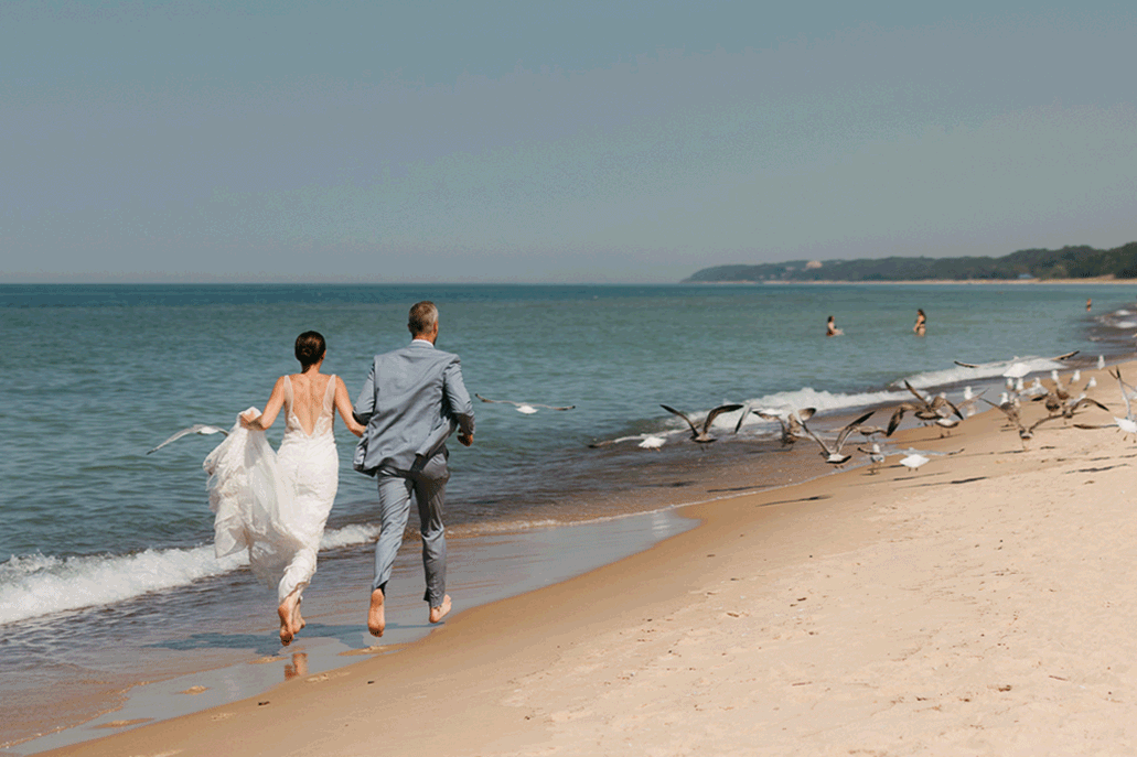 Bride and groom running along the beach of Lake Michigan through a flock of seagulls during their elopement at Warren Dunes State Park