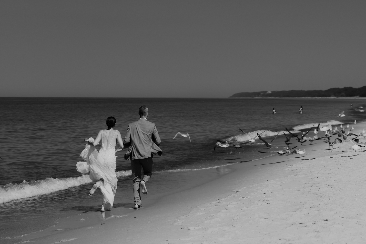 Bride and groom running along the beach shore through a flock of seagulls during their elopement at Lake Michigan